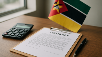 Documentos de contratação pública sobre mesa de escritório com calculadora e bandeira moçambicana ao fundo