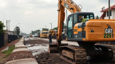 Trabalhadores da construção civil operando escavadora em canal de drenagem urbana sob céu nublado.