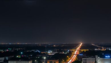 Vista panorâmica noturna de uma metrópole iluminada sob um céu escuro com feixes de luz de segurança