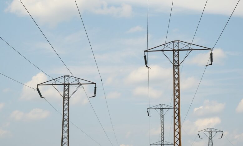 Linhas de alta tensão e postes de distribuição eléctrica sob céu aberto em paisagem moçambicana rural