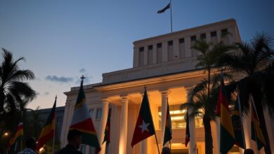 Bandeiras diplomáticas hasteadas em frente a um edifício institucional sob iluminação suave de final de tarde.