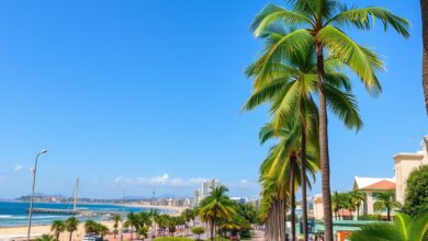 Vista panorâmica da orla marítima de Maputo com calçadão, palmeiras e pequenas estruturas comerciais voltadas ao turismo.
