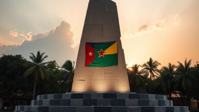 Monumento público de pedra com bandeira nacional ao fundo sob céu límpido ao entardecer.